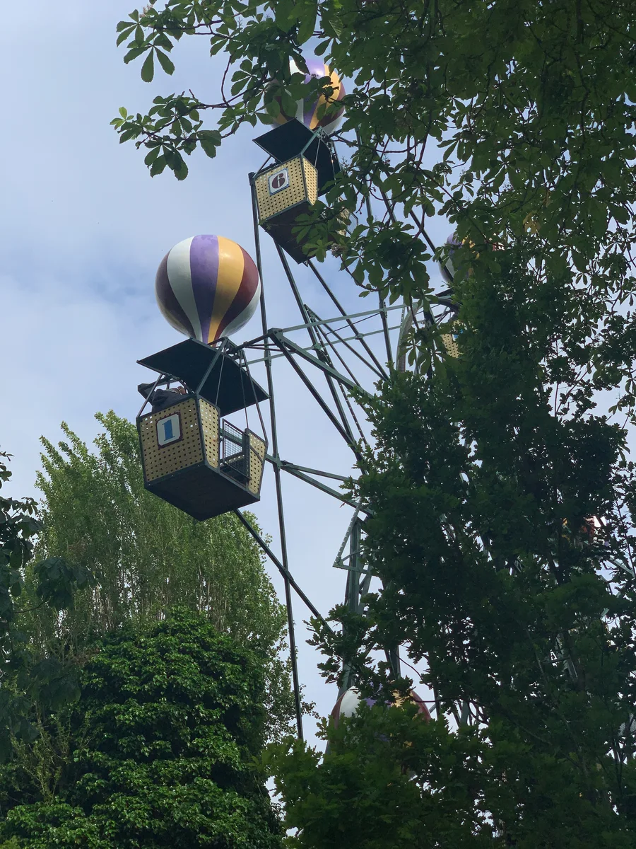 A balloon-themed amusement ride rising among leafy trees