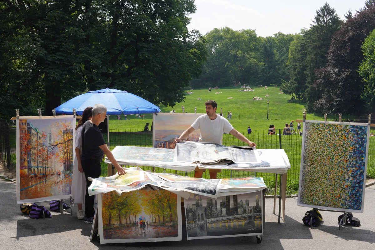 An artist displaying paintings beneath an umbrella in the park