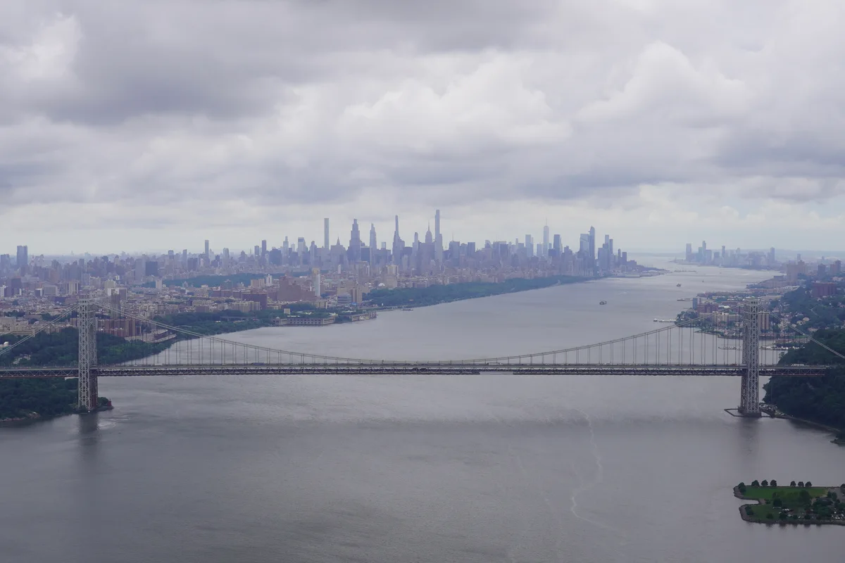 An aerial view of the George Washington Bridge and the Manhattan skyline beneath clouds
